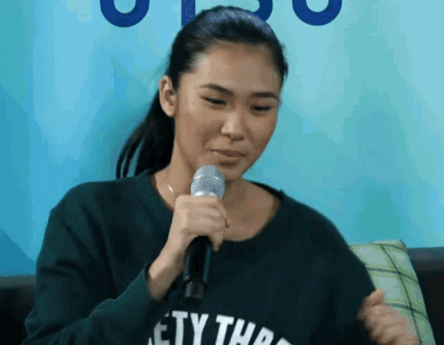 a woman is holding a microphone and wearing a sweater that says " society "