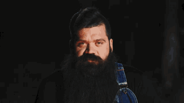 a man with a long beard wearing overalls looks at the camera