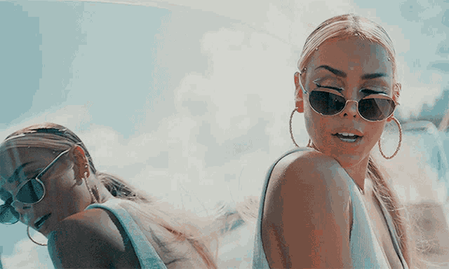 a woman wearing sunglasses and hoop earrings looks over her shoulder