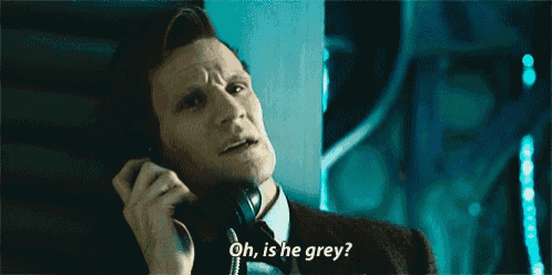 a man in a suit and tie is talking on a phone and says oh is he grey .
