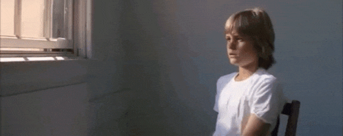 a young boy in a white shirt is sitting in a chair in front of a window .