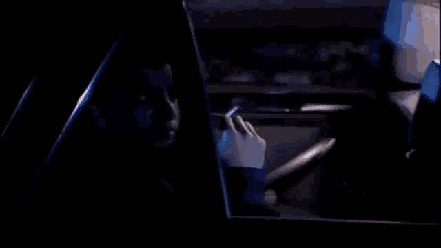 a man is smoking a cigarette while sitting in a car at night .