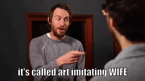 a man with a beard is pointing at himself in a mirror and says it 's called art imitating wife