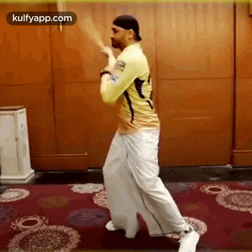 a man in a yellow shirt and white pants is holding a bat and dancing .
