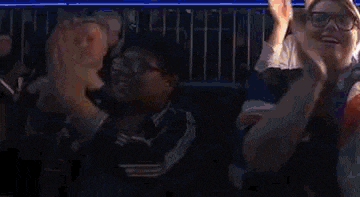a group of people are sitting in a stadium applauding a game .