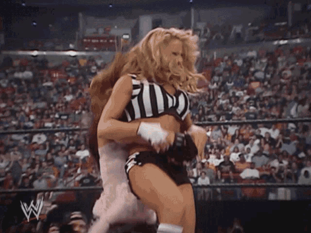 a woman in a referee 's uniform is wrestling another woman in a wrestling ring