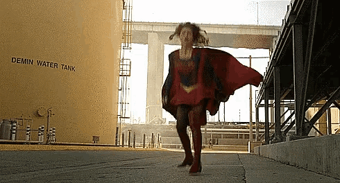 a woman in a superhero costume is walking in front of a large demin water tank