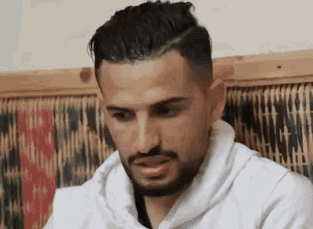 a man with a beard is wearing a white sweater and sitting on a chair .