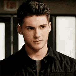 a young man wearing a black shirt and a black jacket is standing in front of a door .