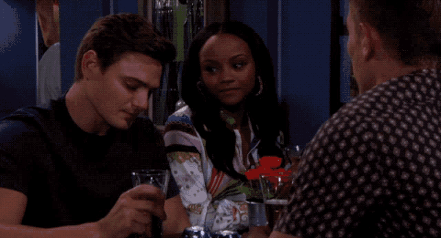 two men and a woman are sitting at a table with a glass of beer in front of them