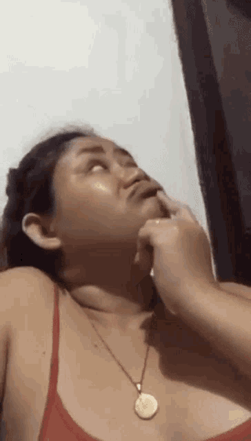 a woman wearing a red bra and a gold necklace is touching her face with her hand .