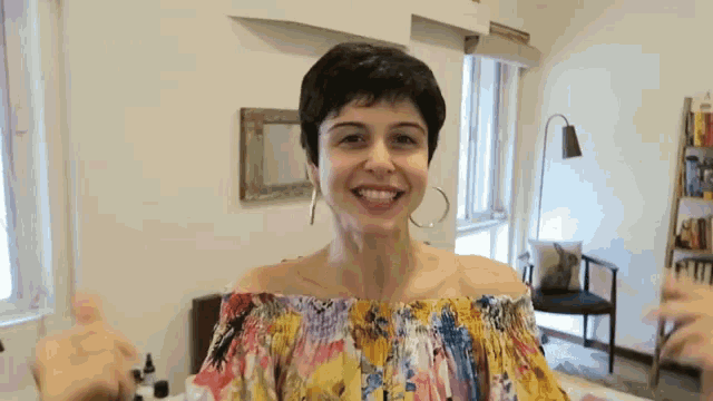 a woman in a colorful off the shoulder top is smiling and giving a thumbs up