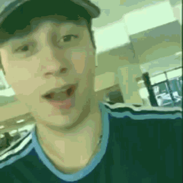 a young man wearing a hat and a blue shirt is taking a selfie