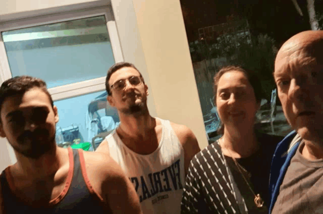a man wearing a tank top that says palmetto is standing next to two other men and a woman