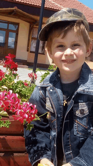 a young boy wearing a hat and a denim jacket is smiling