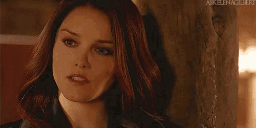 a woman with red hair and green eyes is leaning against a wall and looking at the camera .