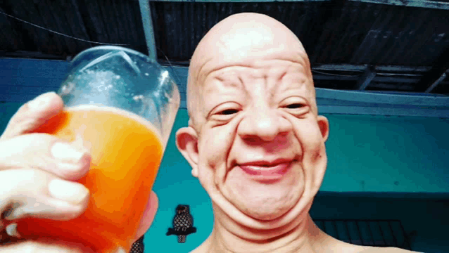 a bald man holds a glass of orange juice in front of his face