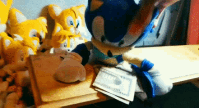 a sonic the hedgehog stuffed animal sits on a table with a stack of money