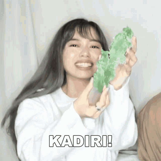 a woman is holding a green object with the word kadiri written on it