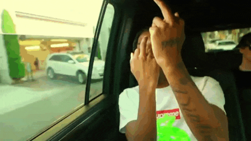 a man in a supreme shirt is giving the middle finger while sitting in a car .