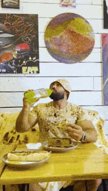 a man sitting at a table drinking from a bottle with the word fat on the wall