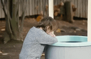 a little girl is leaning against a well and drinking water from it .