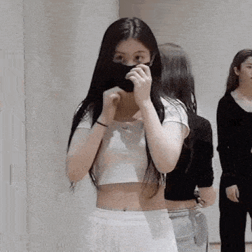 a girl wearing a crop top and a black mask is standing in a room .