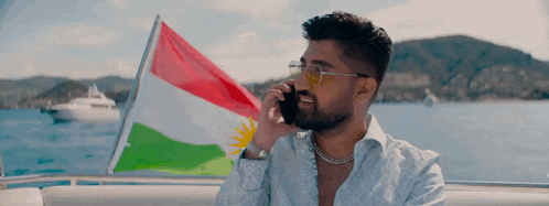 a man on a boat talking on a cell phone in front of a kurdish flag