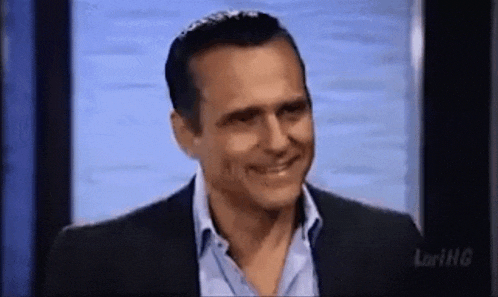 a man in a suit and blue shirt is smiling while standing in front of a blue wall .