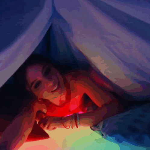 a woman laying under a blanket with a rainbow light