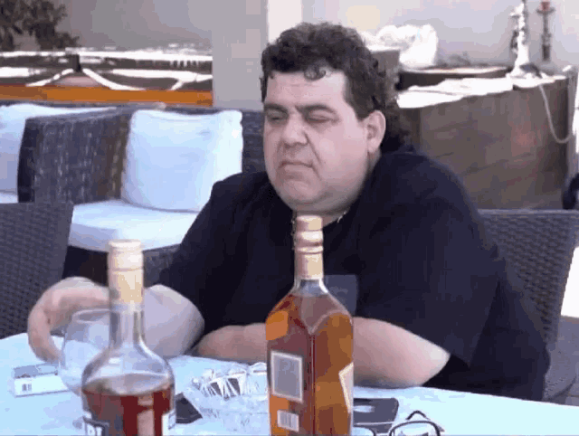 a man sitting at a table with a bottle of alcohol and a glass