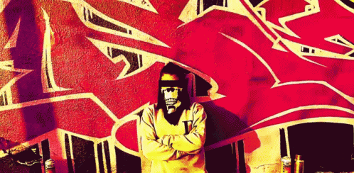 a man wearing a skull mask is standing in front of a wall with graffiti on it