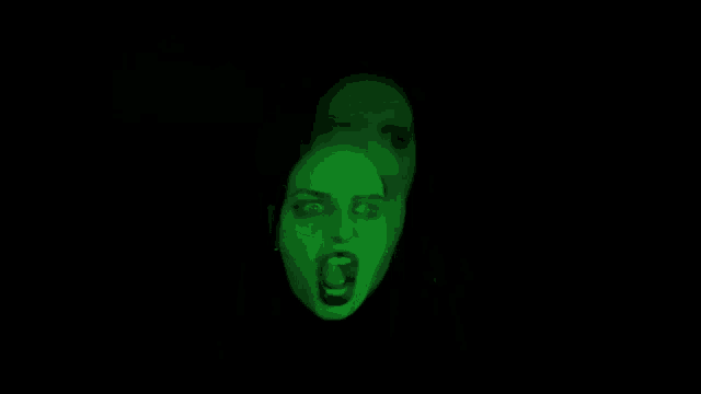 a woman 's face is glowing in the dark with a green light behind it .
