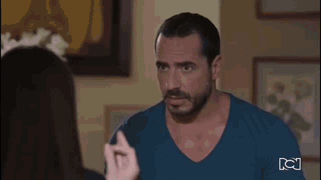 a man with a beard and mustache is talking to a woman in a living room .