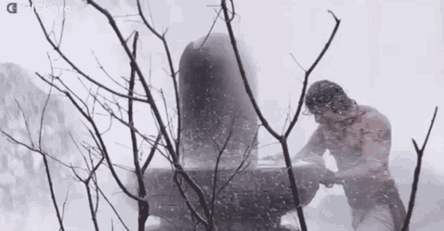 a man is kneeling down in the snow next to a large stone .