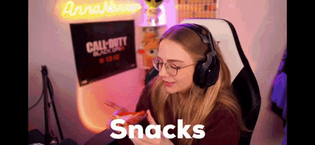 a woman wearing headphones and glasses is eating snacks in front of a call of duty black ops sign