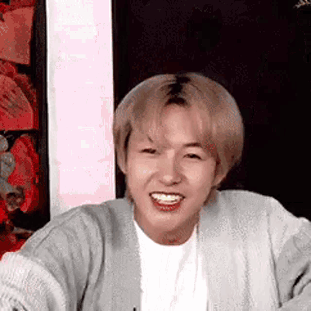 a young man wearing a gray cardigan and a white shirt is smiling for the camera .