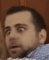 a man with a surprised look on his face is wearing a blue and white plaid shirt .