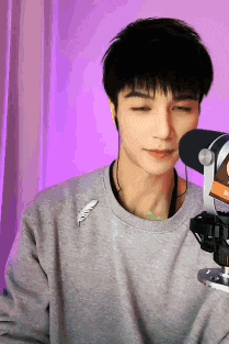a man wearing a gray sweater is standing in front of a microphone with his eyes closed