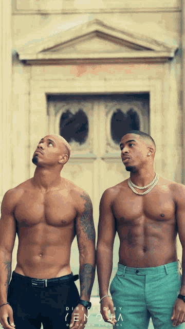 two shirtless men standing next to each other in front of a building that says densha on it