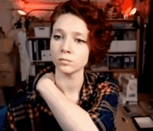 a woman with red hair is wearing a plaid shirt and has her hand on her shoulder