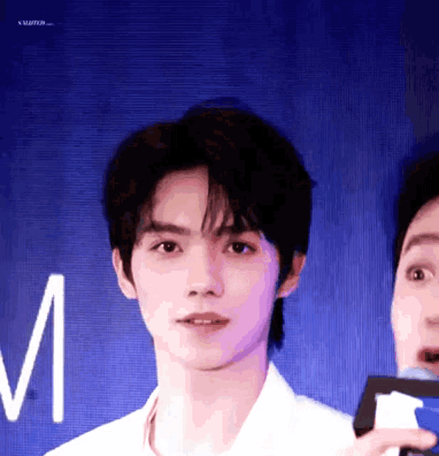 a young man in a white shirt is standing next to another man in a blue background .