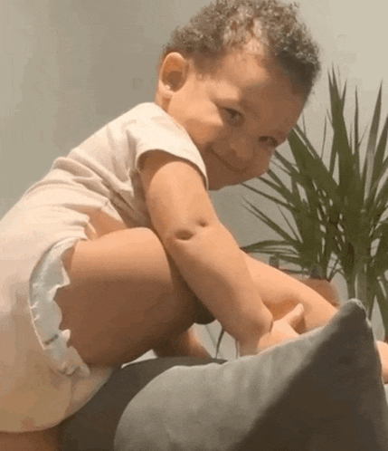 a baby in a diaper is smiling while sitting on a pillow .