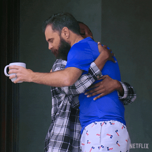 a man in a blue shirt is hugging another man who is holding a cup
