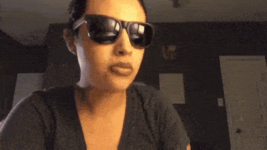 a woman wearing sunglasses in front of a wall that says love