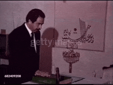 a man in a suit and tie is standing in front of a wall with arabic calligraphy on it .