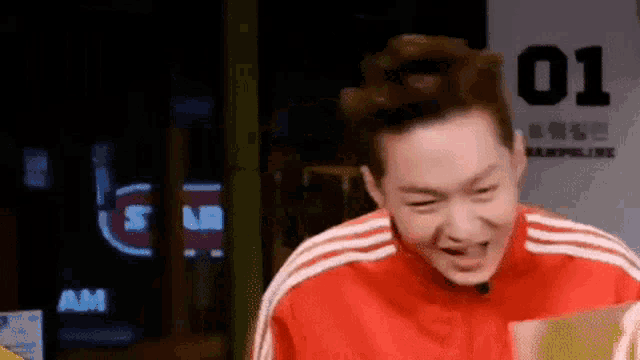 a man in a red jacket is making a funny face while standing in front of a trampoline park .