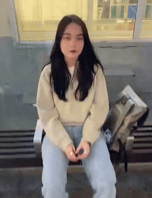a woman is sitting on a bench with her hands folded in front of her face