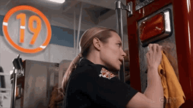 a woman is cleaning a fire truck with the number 19 in the background