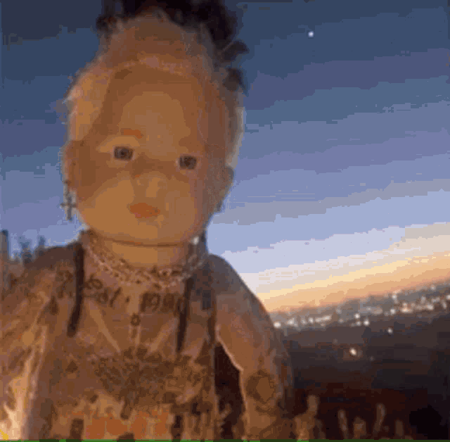 a doll with a tattoo on her chest is standing in front of a city at sunset .